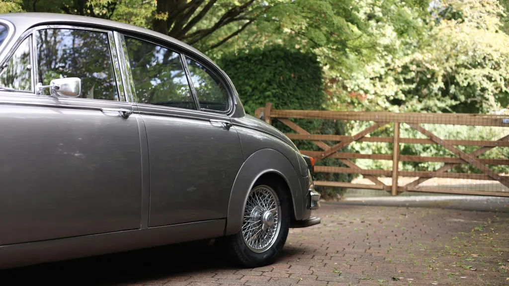 Close-up side view of a silver classic Jaguar Mk2 showing its rear door and wire-spoke wheel