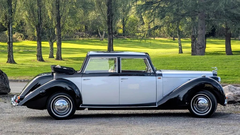 Side profile of an ivory and black Royale Windsor wedding car with its landaulette roof open.