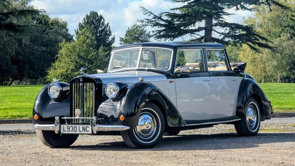 Ivory and black vintage-style Royale Windsor Landaulette wedding car parked beside landscaped gardens.