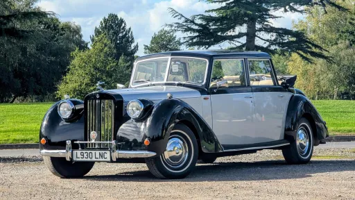 Ivory and black vintage-style Royale Windsor Landaulette wedding car parked beside landscaped gardens.