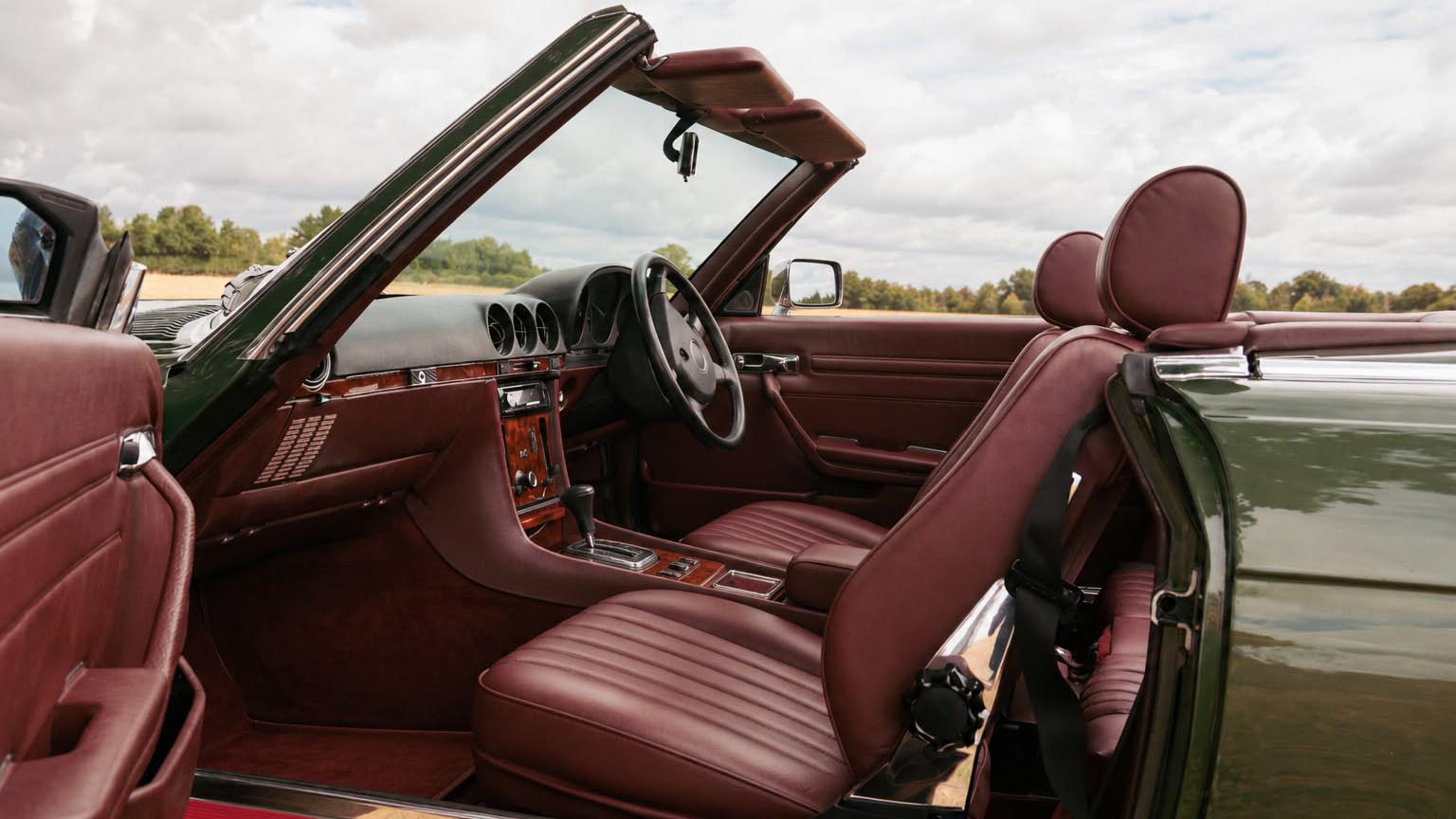 Burgundy leather seats and wooden dashboard inside a 1989 Mercedes-Benz 420 SL with the roof open