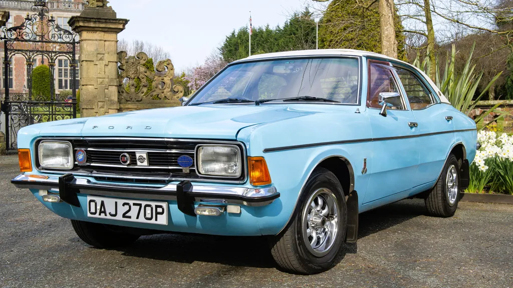 Front three-quarter view of a light blue Ford Cortina Mk4 XLE V6 with a white vinyl roof