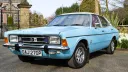 Front three-quarter view of a light blue Ford Cortina Mk4 XLE V6 with a white vinyl roof