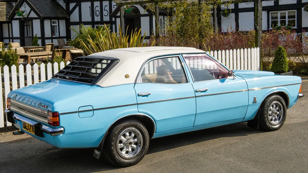 Rear three-quarter view of a light blue Ford Cortina with a white vinyl roof and rear window louvres