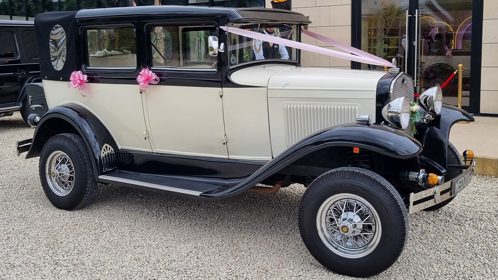 Side view of a cream and black Badsworth wedding car with pink bows at Halo Mansion