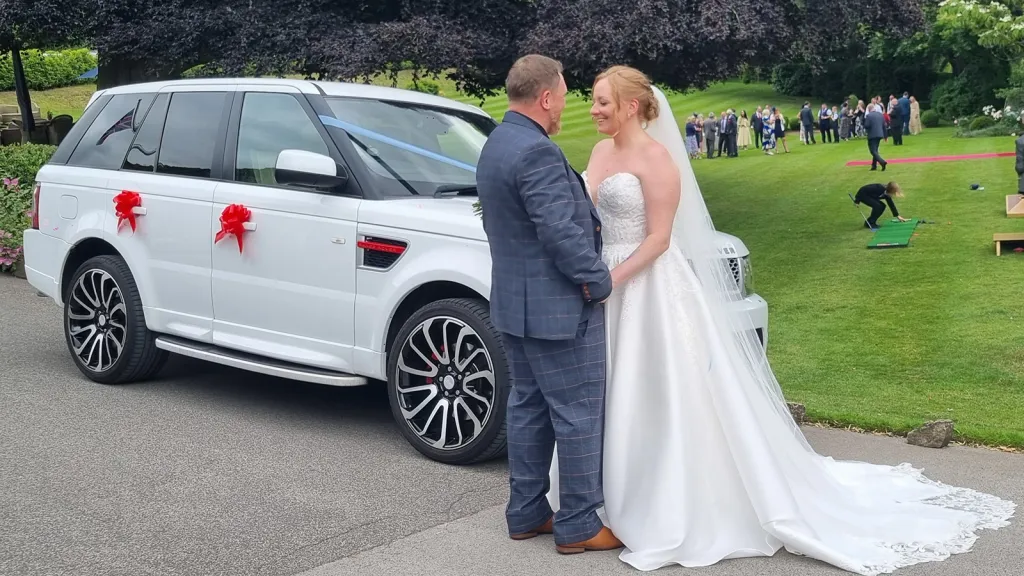 Bride and groom beside a white Range Rover Sport Autobiography decorated with red wedding bows
