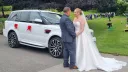 Bride and groom beside a white Range Rover Sport Autobiography decorated with red wedding bows