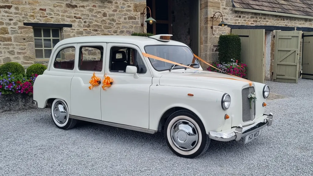 Ivory classic wedding taxi with orange ribbons outside The Tithe Barn at Bolton Abbey