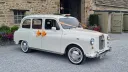 Ivory classic wedding taxi with orange ribbons outside The Tithe Barn at Bolton Abbey