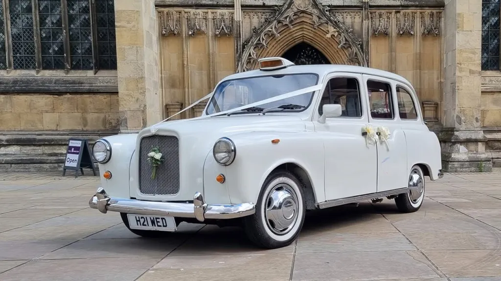 Front three-quarter view of an ivory classic London taxi outside a Yorkshire cathedral