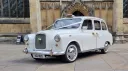 Front three-quarter view of an ivory classic London taxi outside a Yorkshire cathedral