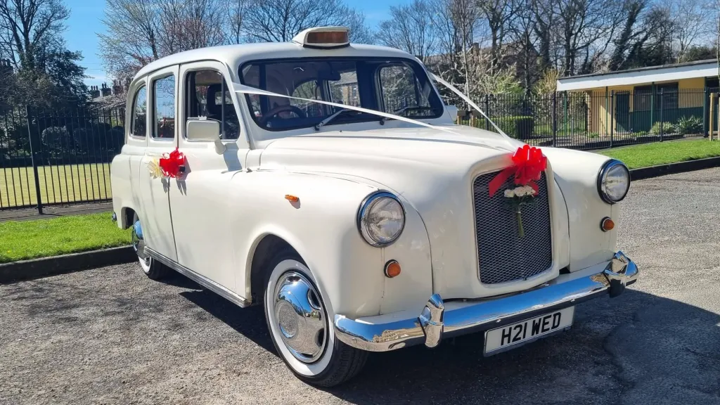Ivory classic wedding taxi decorated with red ribbons and bows