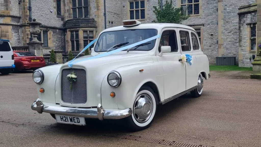 Cream-coloured classic London taxi with white wedding ribbons outside a stone venue