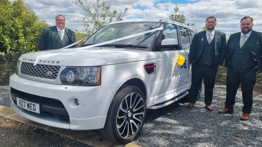 Groomsmen beside a white Range Rover Sport Autobiography decorated with yellow wedding bows