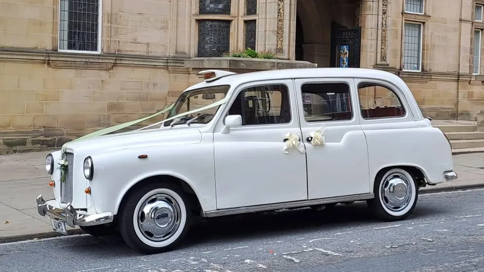 Side view of an ivory classic London taxi decorated with white wedding bows