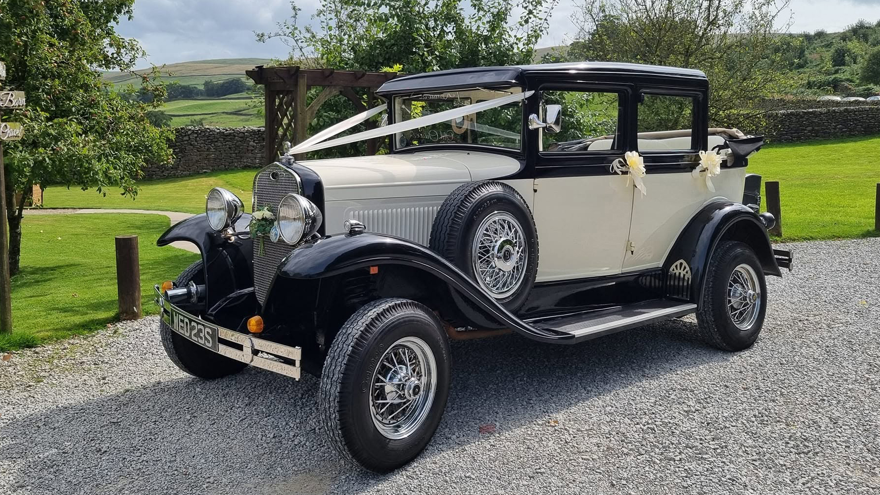 Cream and black Badsworth Landaulette wedding car parked beside a lawn in Yorkshire