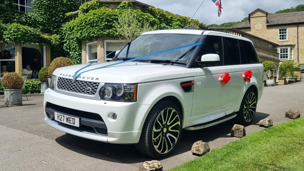 White Range Rover Sport Autobiography decorated with blue ribbons and red wedding bows outside a wedding venue