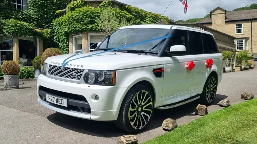 White Range Rover Sport Autobiography decorated with blue ribbons and red wedding bows outside a wedding venue