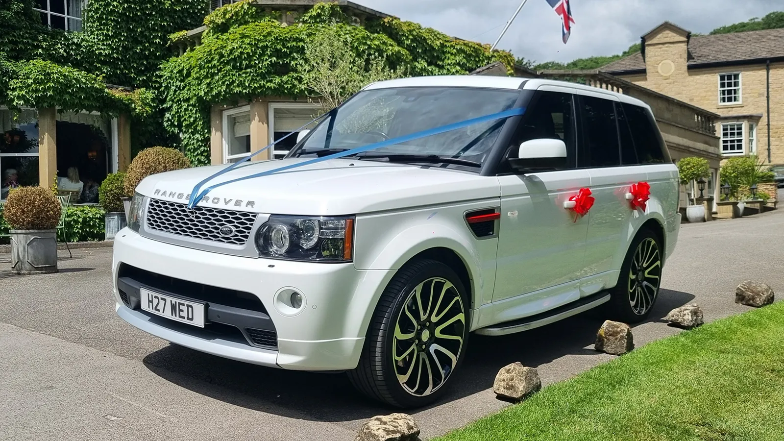 White Range Rover Sport Autobiography decorated with blue ribbons and red wedding bows outside a wedding venue