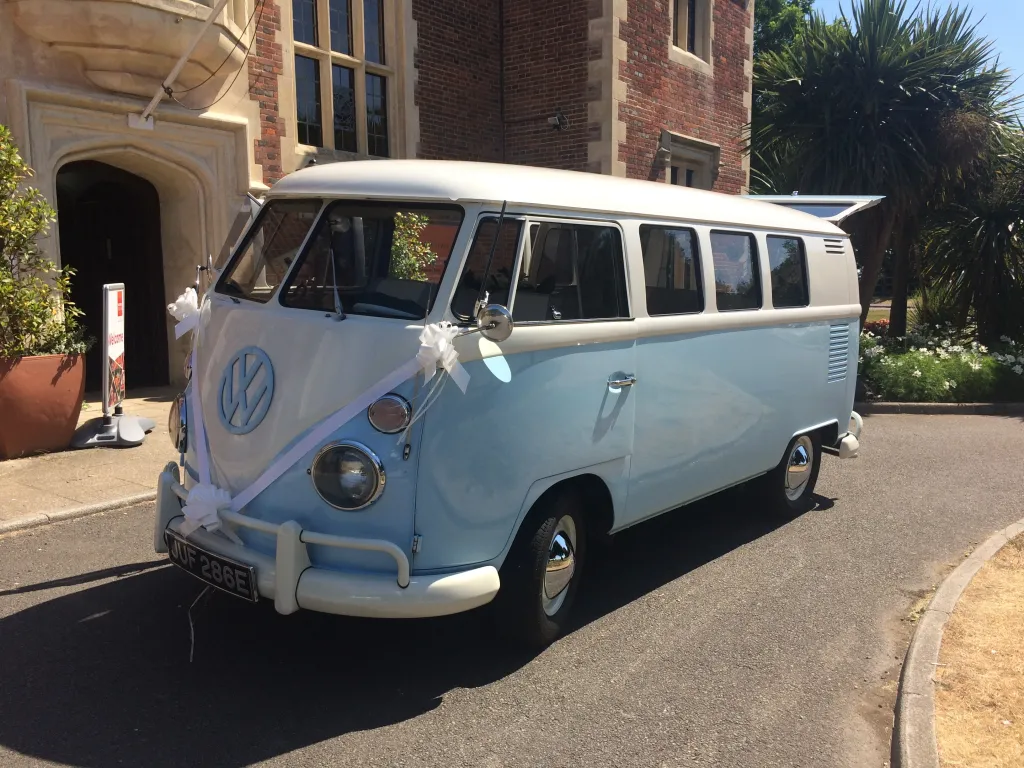 Classic Volkswagen campervan in Blue and White in decorated with white ribbons across its front bonnet.  