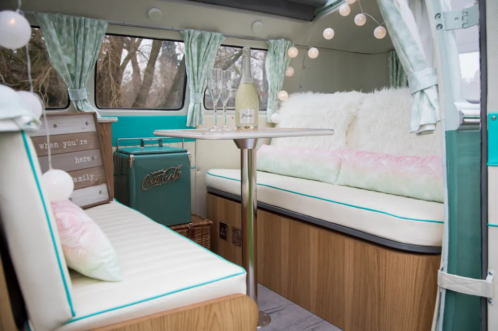 Rear interior of campervan showing bench seats in white leather facing each others. Bench seats can seat up to 3 each.  Pastel Green Curtains and divers wedding decoration