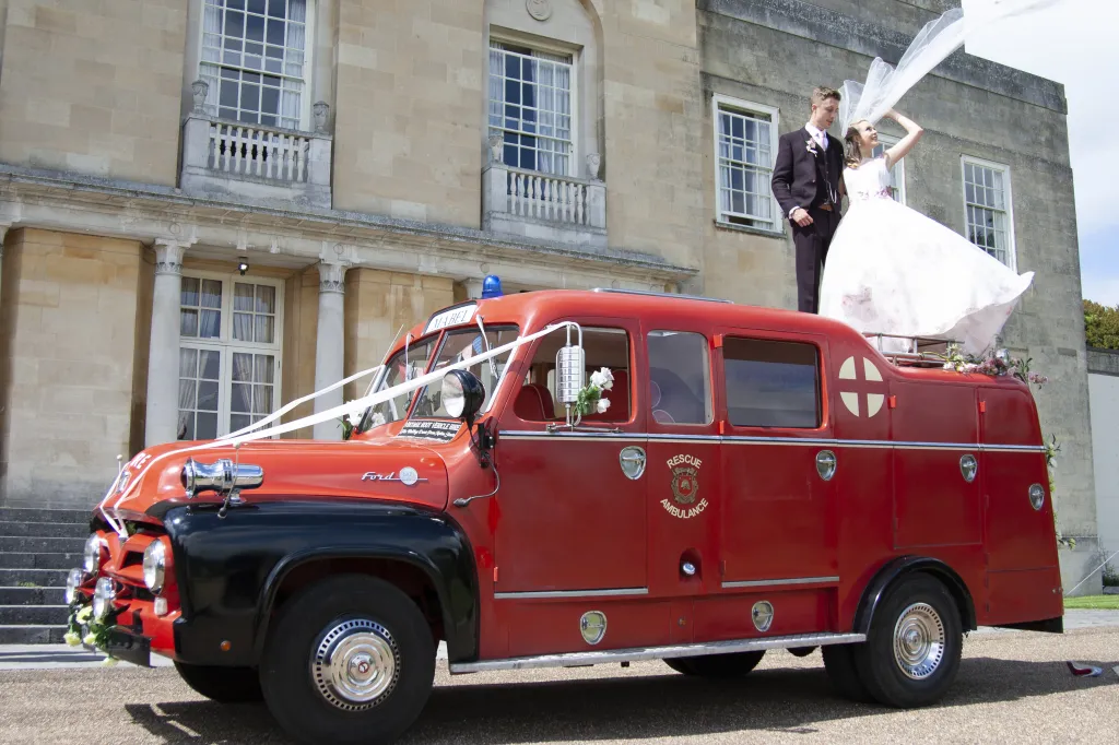Red Fire Truck parked in town with Bride and Groom standing on the vehicle posing for their wedding photographer
