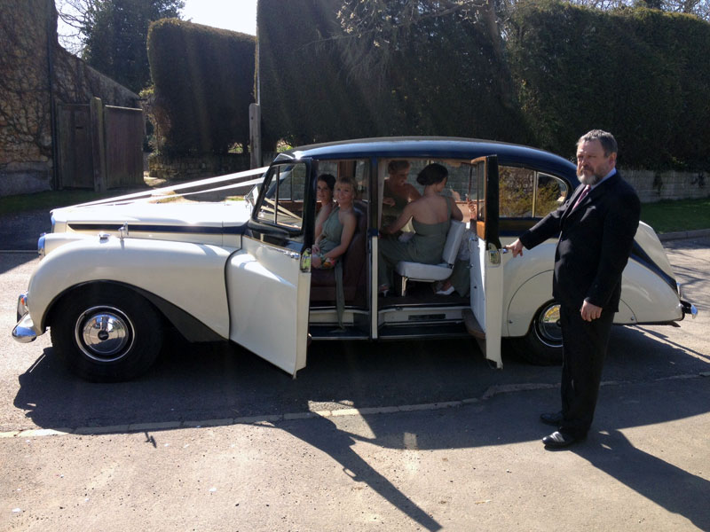 Classic Austin Princess Limousine with Bridesmaids inside the vehicle and chauffeur holding the door. 
