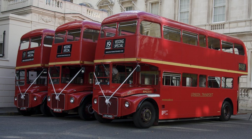 Three identical Red Routemaster buses decorated with matching white ribbons and bow. All buses are aligned in the same position next to each others