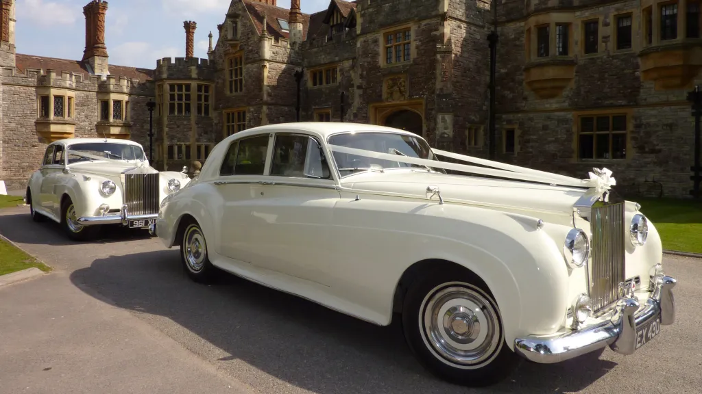 Two Ivory Classic Rolls-Royce silver Clouds decorated with wedding ribbons in front of Rhinefield House Hotel in the New Forest