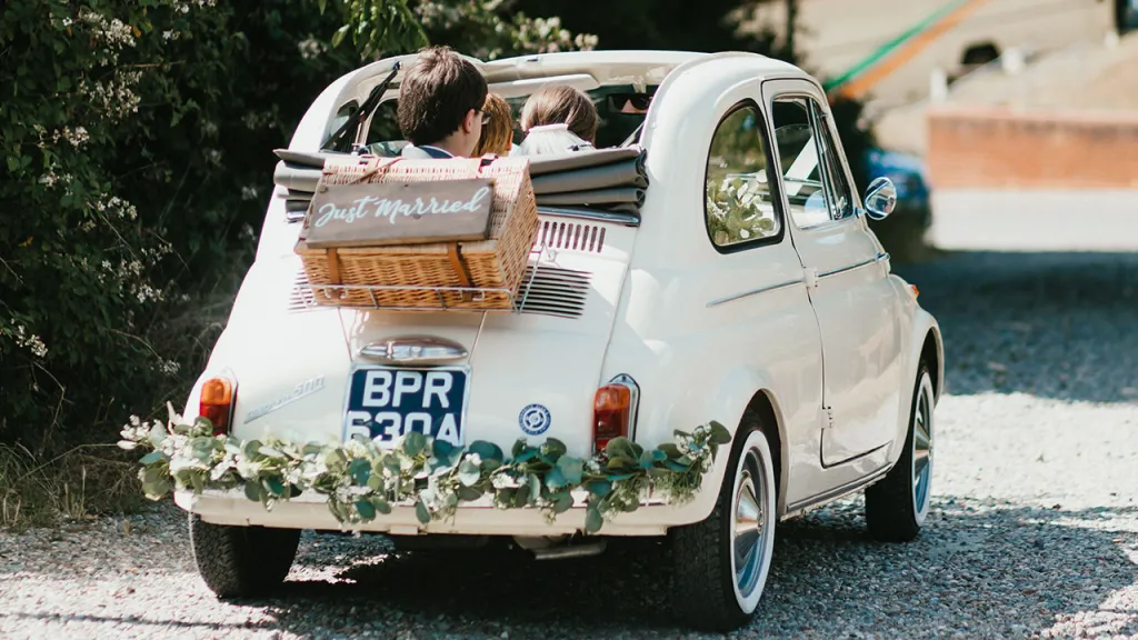 Classic Convertible car with roof down and couple seating in the rear of the vehicle. Vehicle is decorated with a hamper and Just Married sign.