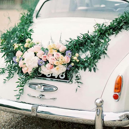 Green Guarland and pink and yellow flowers display attached to the rear boot of a classic wedding car