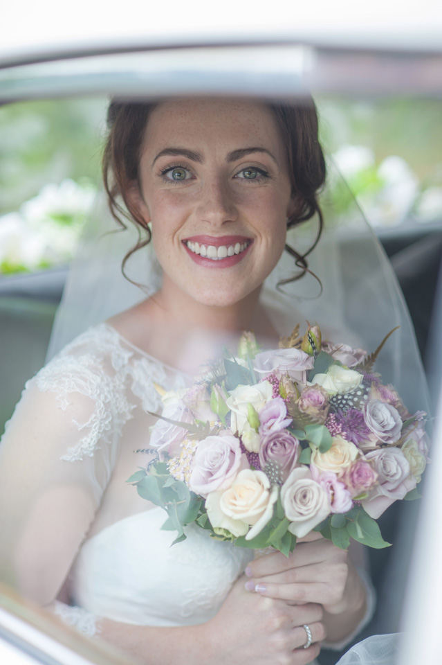 Happy and smiling Bride holding a White and pink bouquet of flowers in the back of a classic car