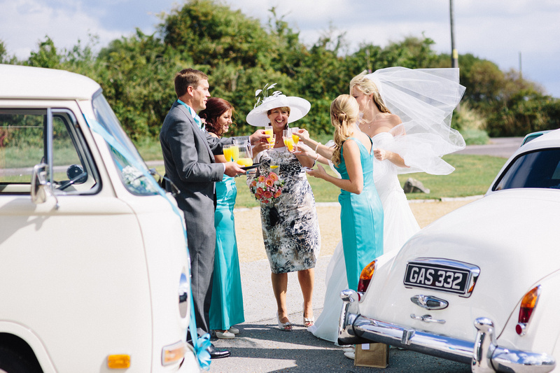 Bride and wedding guiests standing by the classic cars having a glass of Bucks Fizz