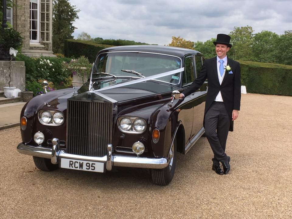 Burgundy Rolls-Royce Phantom dressed with ribbons and groom standing by the vehicle