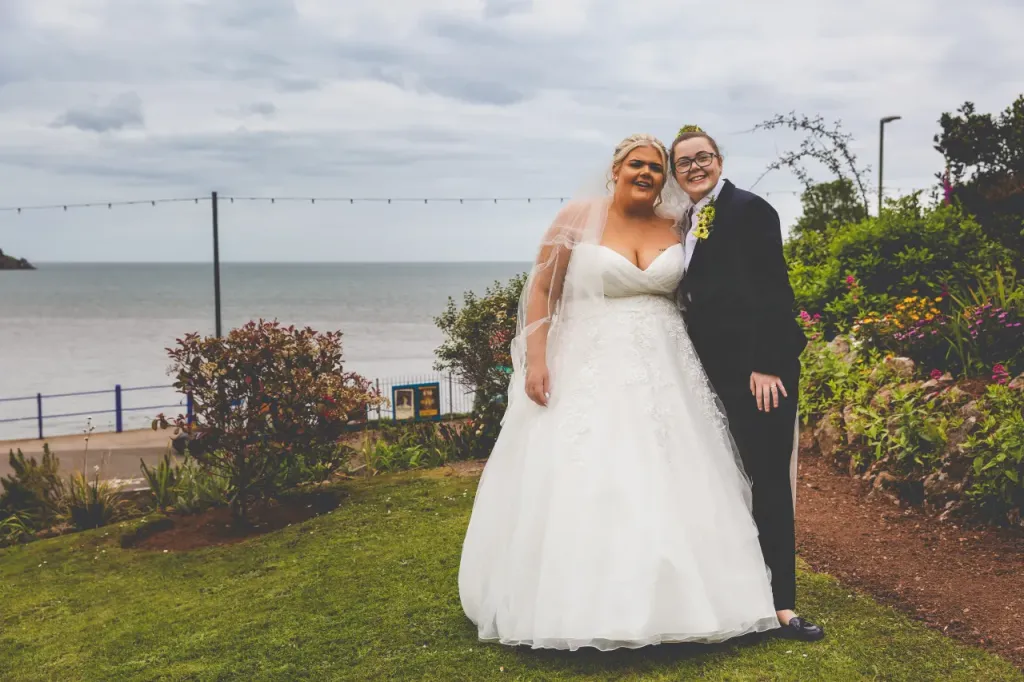 Two brides holding each others in the garden of the Grand Hotel with view of the sea in the background