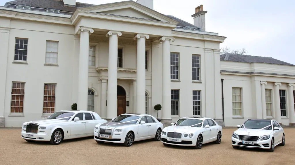 Four white modern wedding cars parked side by side with two Rolls-Royce, one Beltey and one Mercedes. All decorated with matching white ribbons