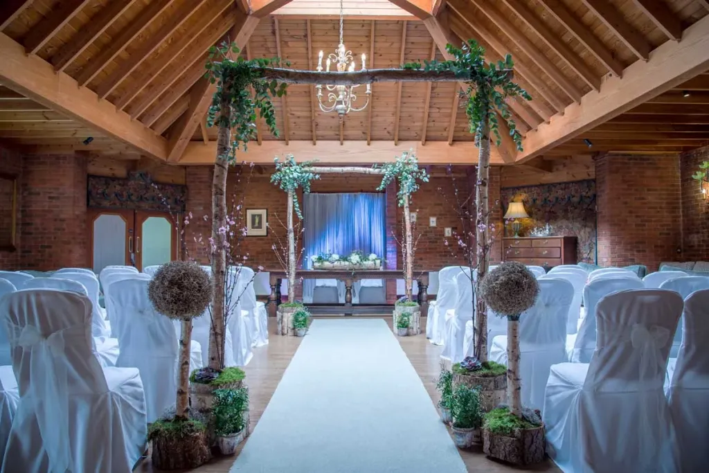 Ceremony Room at Carey's Manor deced with green foliage, wooden chairs and tree made arch 