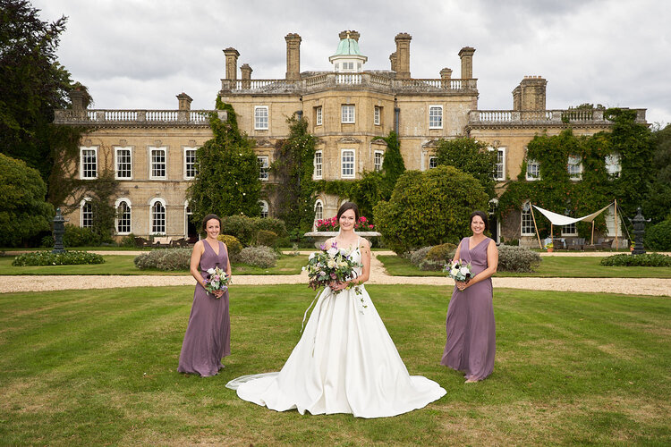 Bride wearing a white wedding gown with her two bridesmaids in the garden of Pylewell House. 
