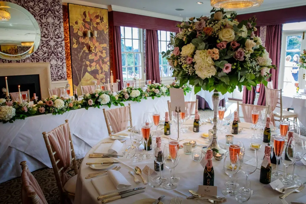 a Colourful wedding breakfast room set up with white flowers, lit-up candles, flute glasses filled with Rose Champagne