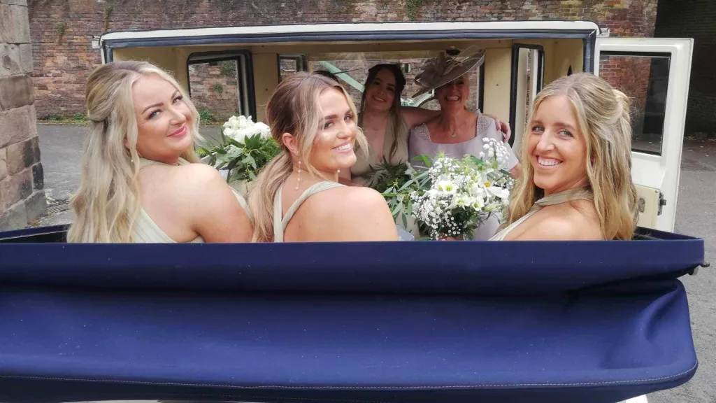 Smiling Bride travelling in a vintage semi-convertible wedding car with her three Bridesmaids and her Mother