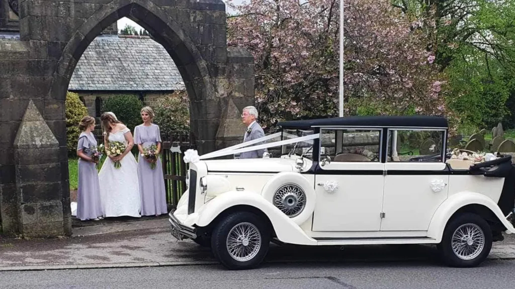 Black & White Regent Convertible with the roof down. Bride and and Bridesmaids can be seen in the background. Vehicle is parked on front of a church.