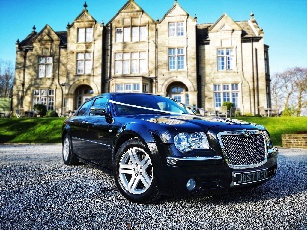 Black American Chrysler 300c Saloon decorated with White ribbons in front of wedding venue