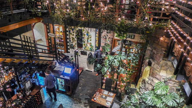 looking down on a busy restaurant space filled with plants and lit with fairy lights.