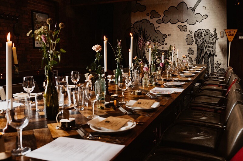 Wooden Table set for dinner with candles, white dinner plates, silver cutlery and menus. 