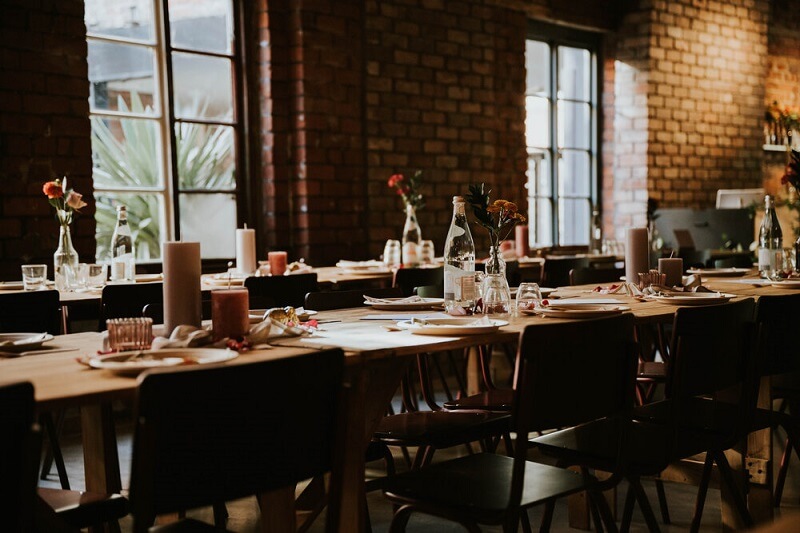 Reception room set-up for wedding breakfast with flowers on the table and brick wall in the background