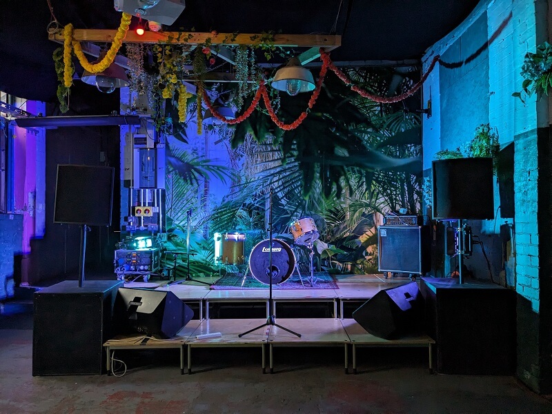 Music Stage set up with drums, speakers and Microphone with a tropic wall photo background and hanging tropical decoration