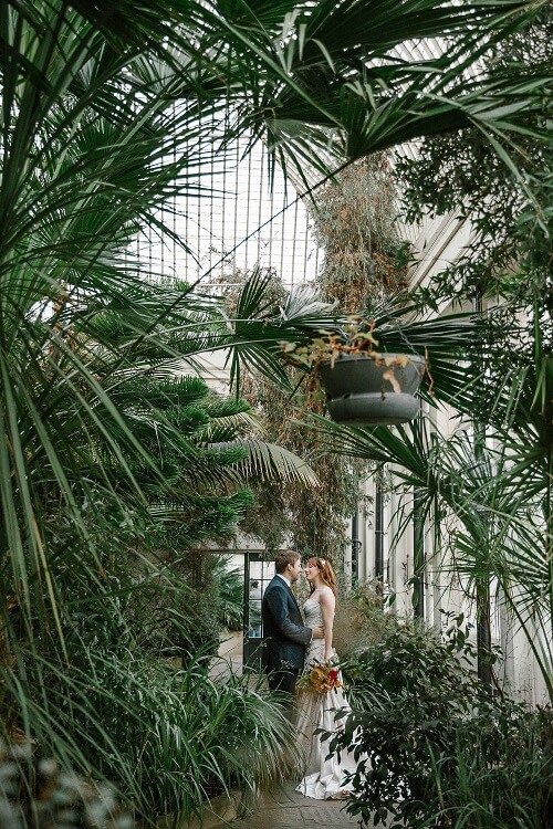 Bride and Groom holding each others in the middle of the Botanical Garden. They are surrounded by green trees and palm trees.