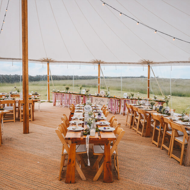 Wooden Tables set-up under a marquee decorated with flowers