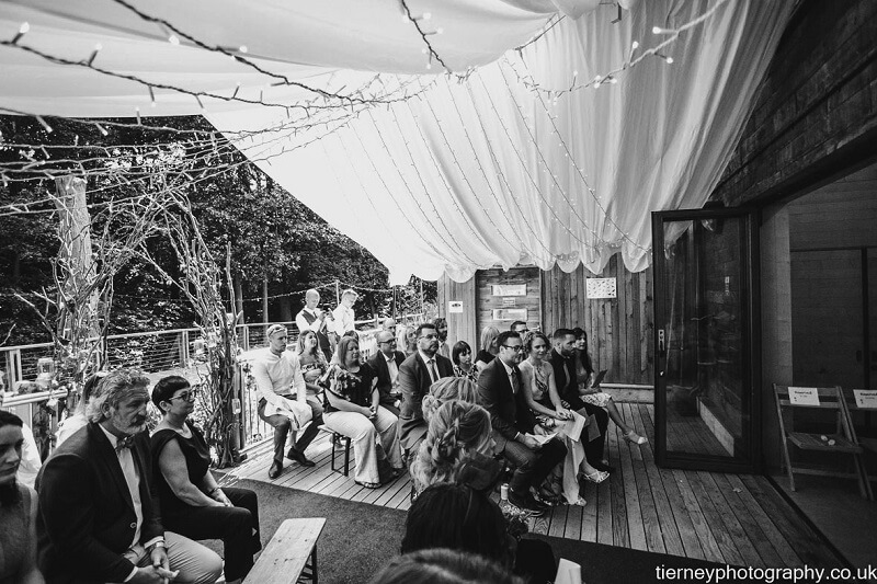 black & white photo os wedding guests seating at the ceremony on the outdoor decking
