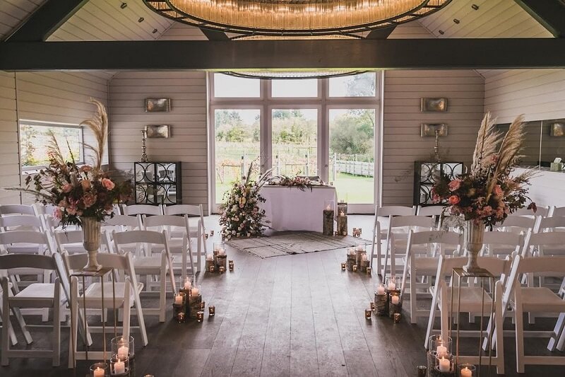 Ceremony Room at Wickham Estate with White Wooden Chairs, lit-up candles in the fllow and flower decoration of pale pink roses